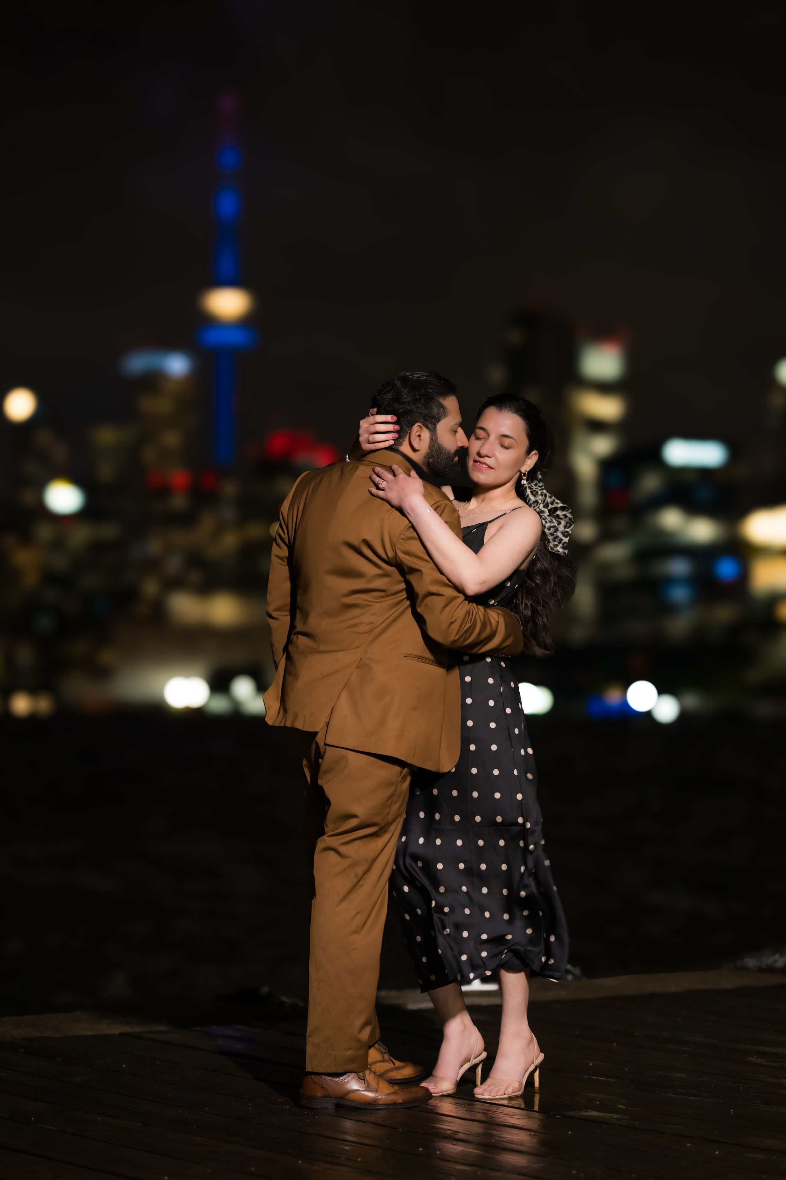 Dancing couple embraces at night with illuminated city skyline and CN Tower in background.