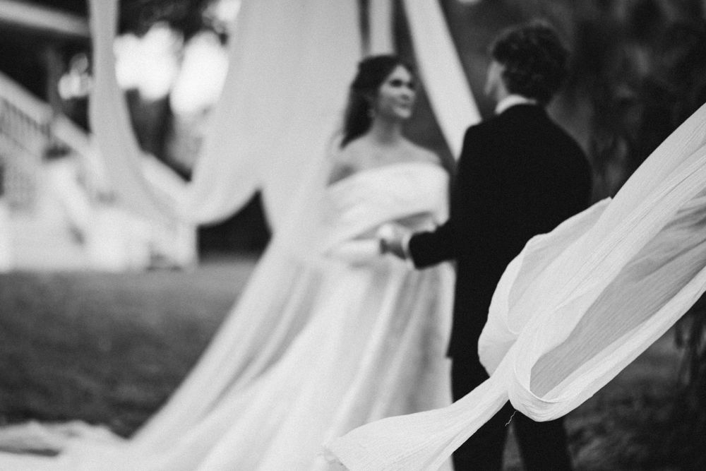 Black and white photo of newlyweds with flowing fabric decorations in foreground.