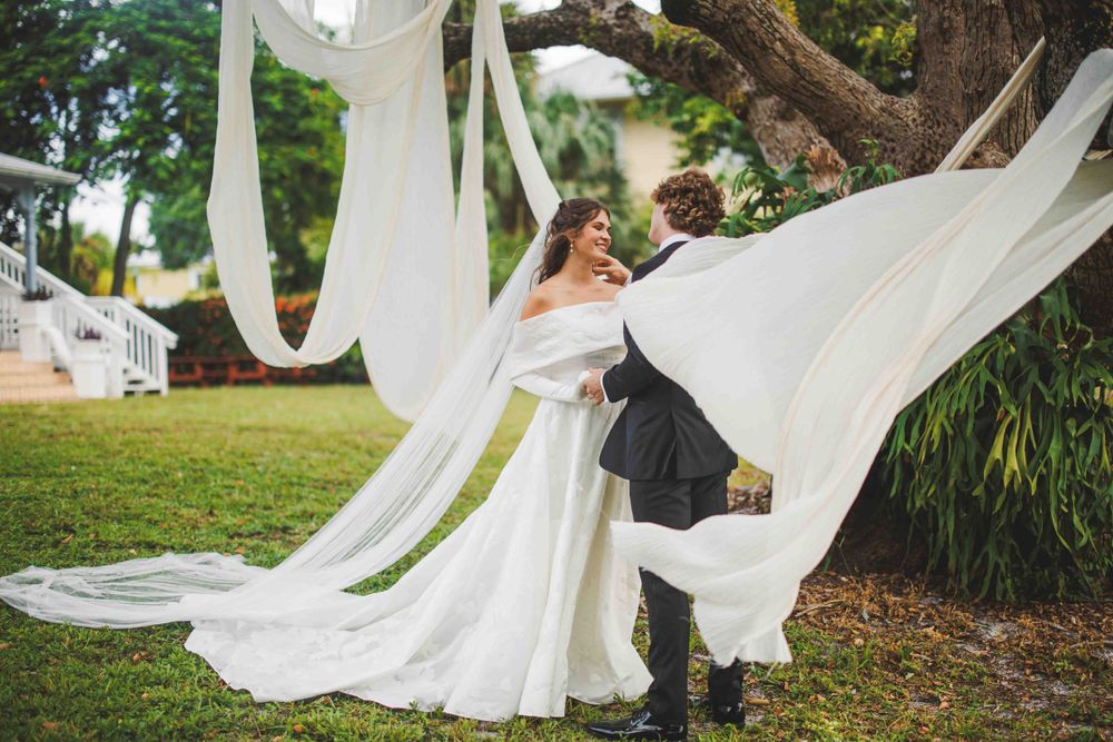 A bride and groom dance with flowing white fabric draping in an outdoor garden setting.