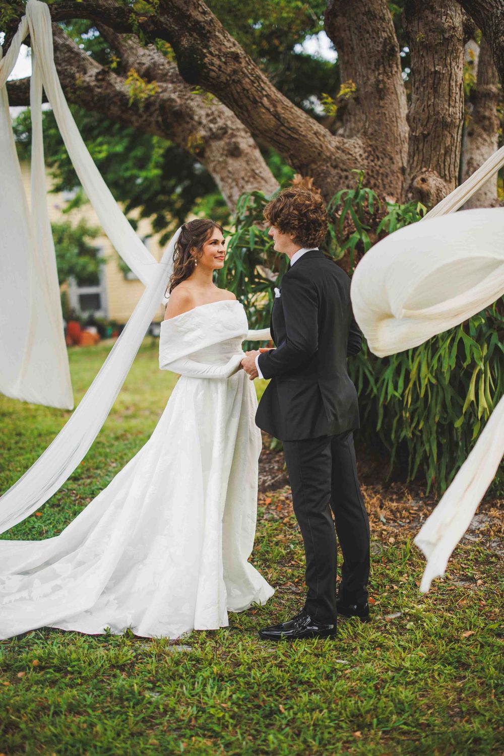 A romantic wedding moment under a tree with flowing white fabric decorations.