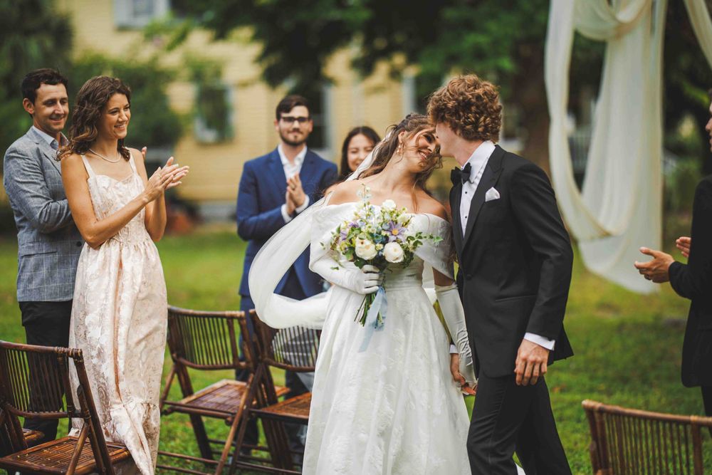 Wedding guests cheer as newlyweds celebrate during an outdoor garden ceremony.