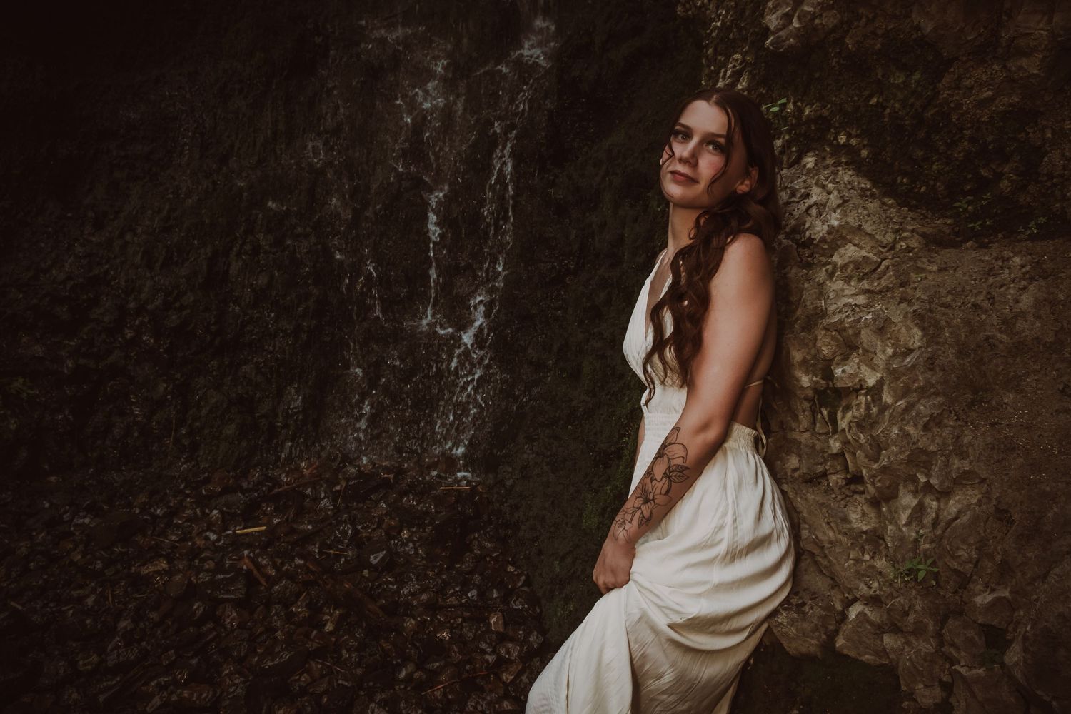 A dramatic portrait against a stone wall wearing a flowing white dress.