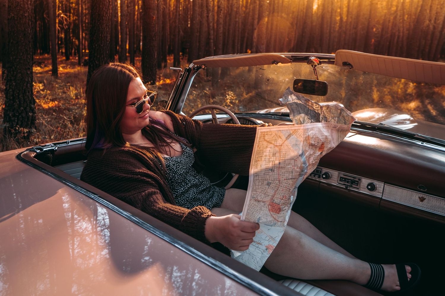 Someone relaxes in a classic convertible car during sunset in a forest setting.