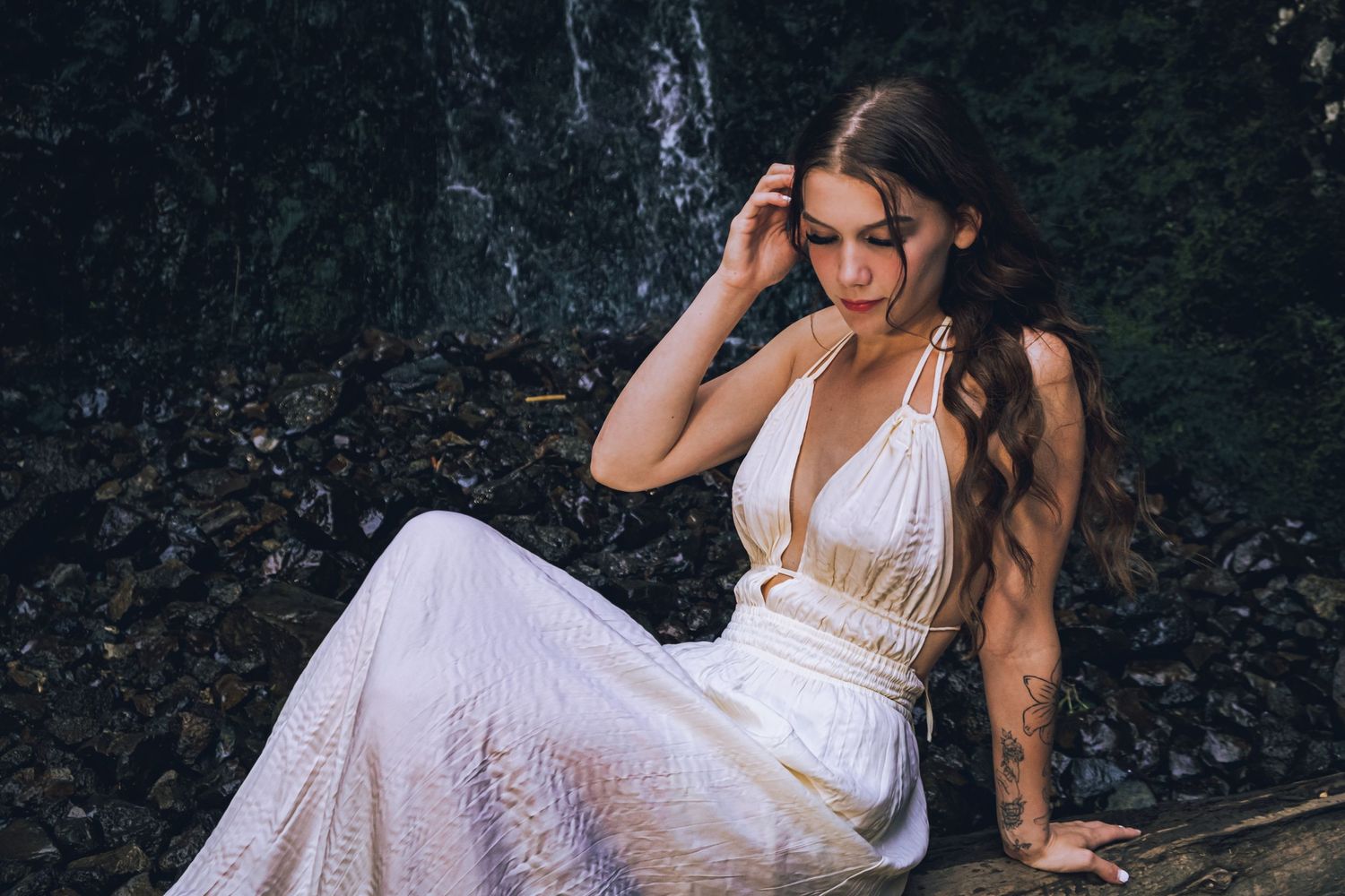 A romantic portrait in a white flowing dress near a waterfall.