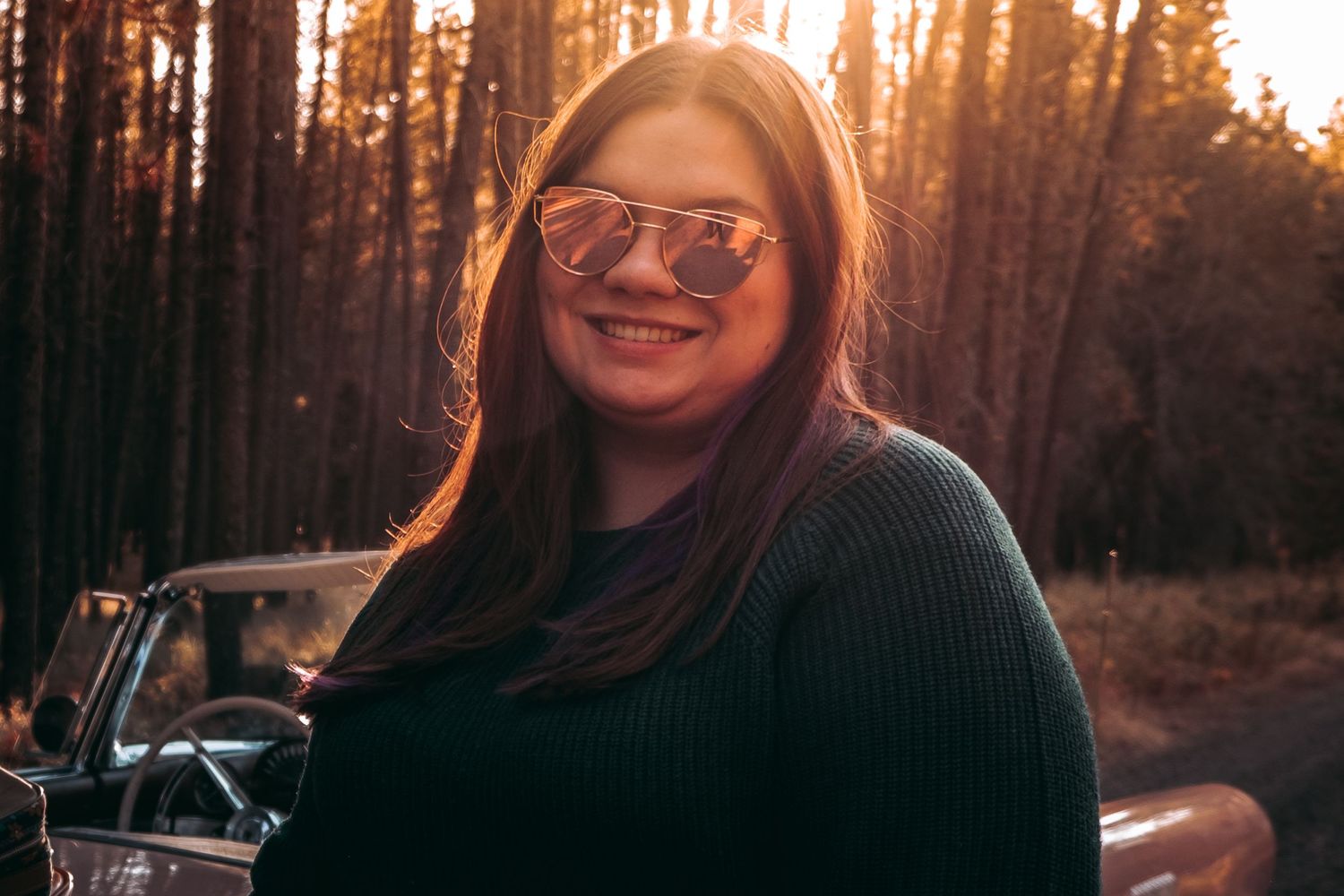 A sunset portrait in a forest featuring sunglasses and a dark sweater.