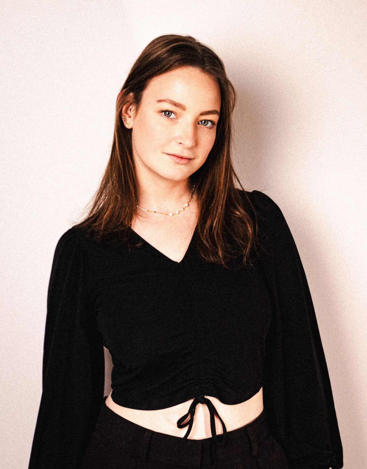 Studio portrait featuring someone in a black crop top with long dark hair against a light background.