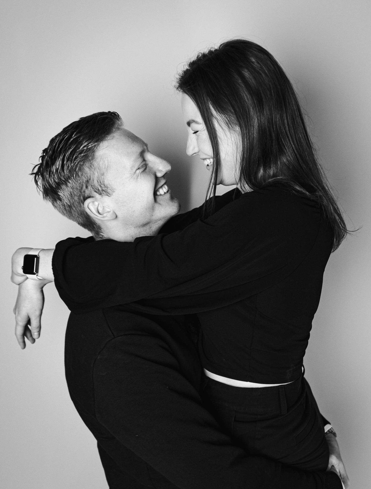 Black and white photo of a couple in dark clothing embracing and smiling.