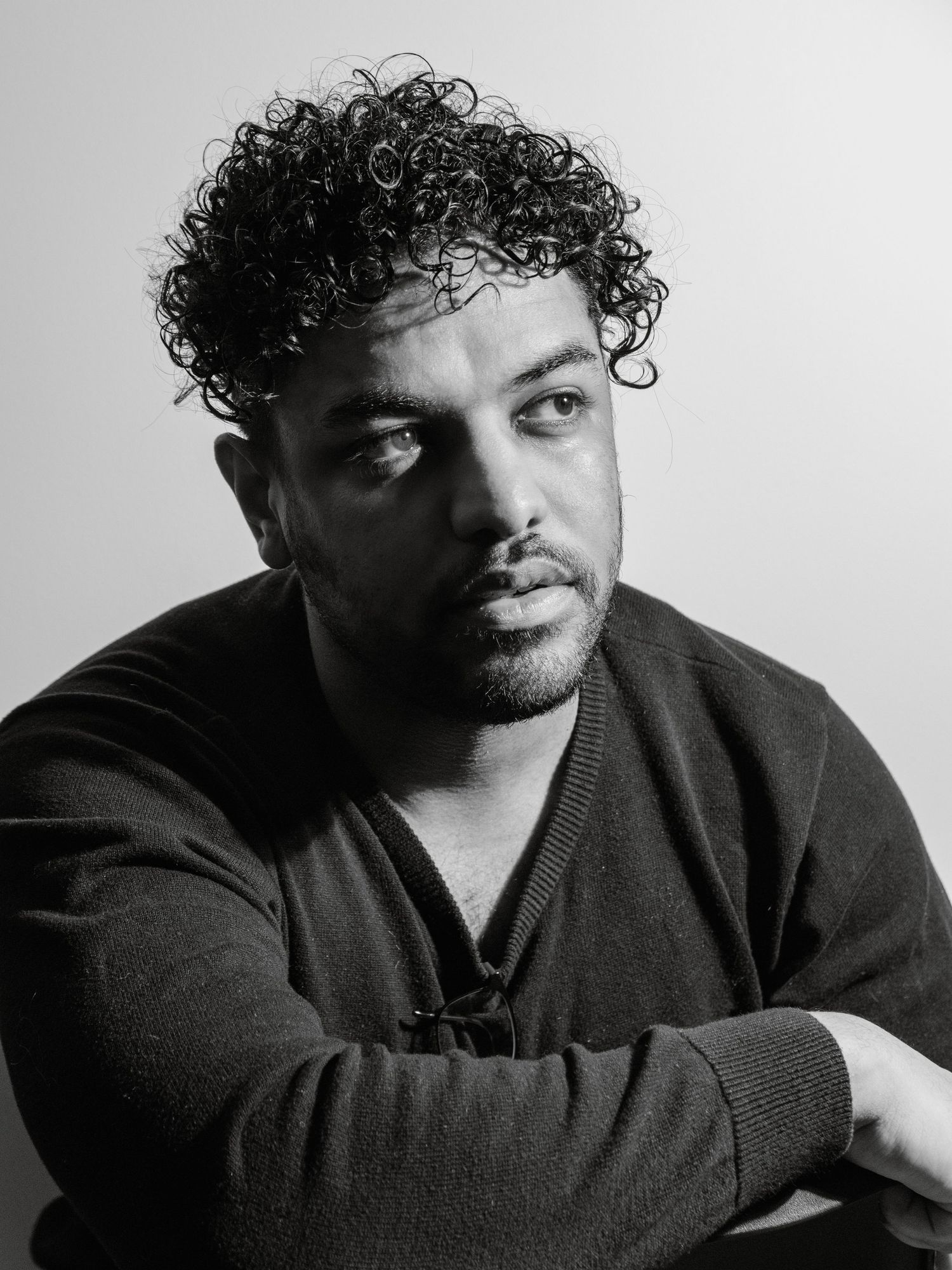 Black and white portrait of person with curly hair wearing dark sweater.
