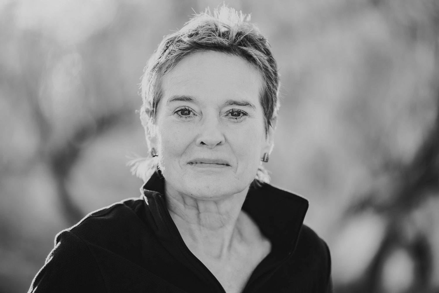Black and white portrait of a person in a dark jacket, looking directly at camera with short cropped hair.
