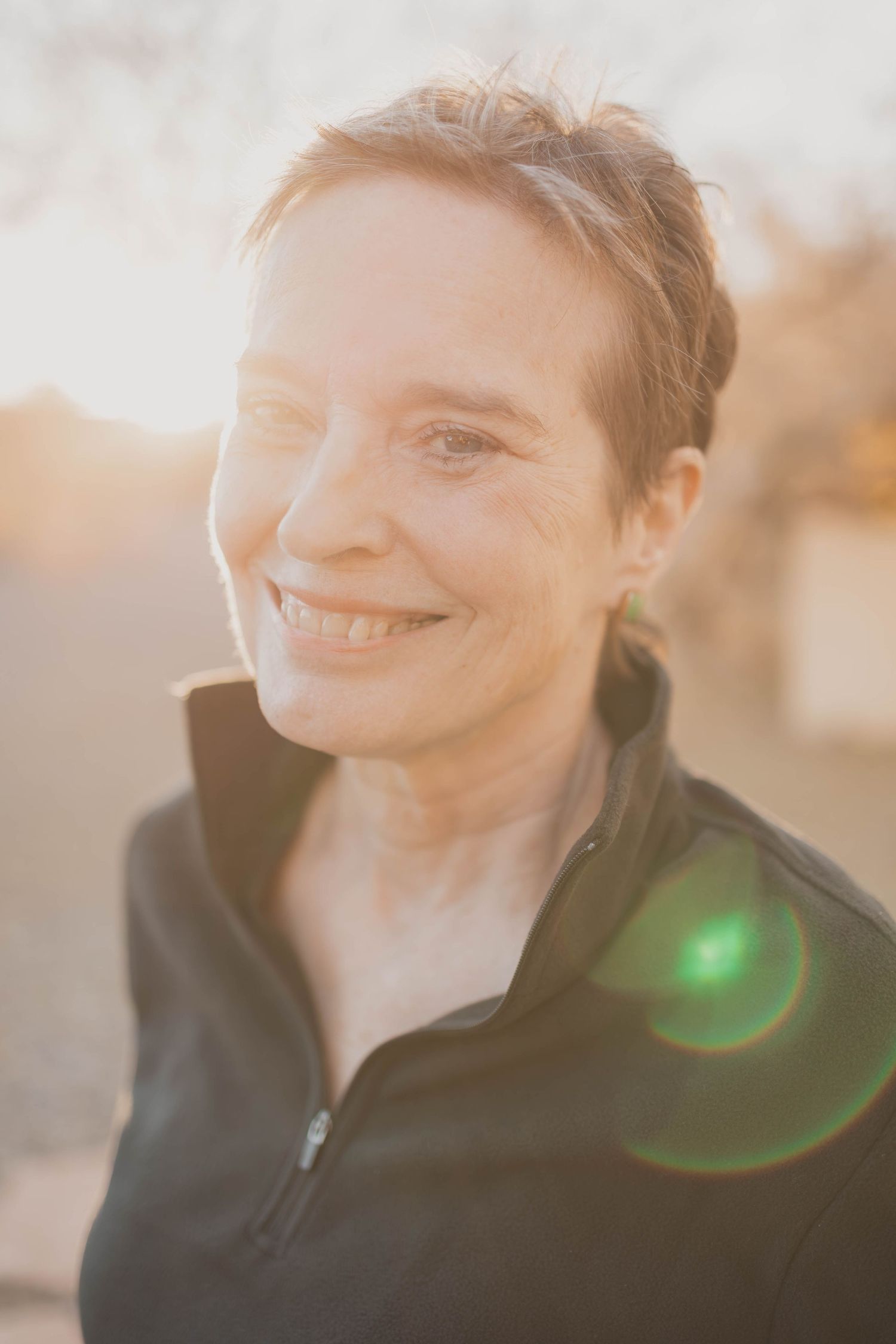 A close-up portrait with natural sunlight creating warm tones and lens flare effect against a blurred background.