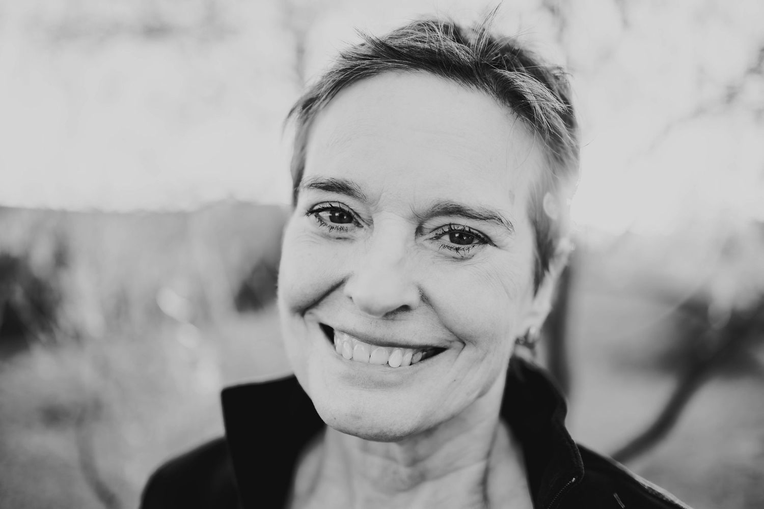 Black and white portrait of someone with short hair and a bright genuine smile looking at camera.