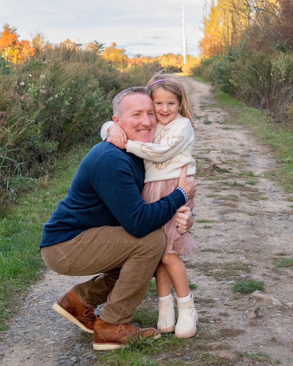 A sweet embrace shared on a dirt path surrounded by autumn foliage and golden light.