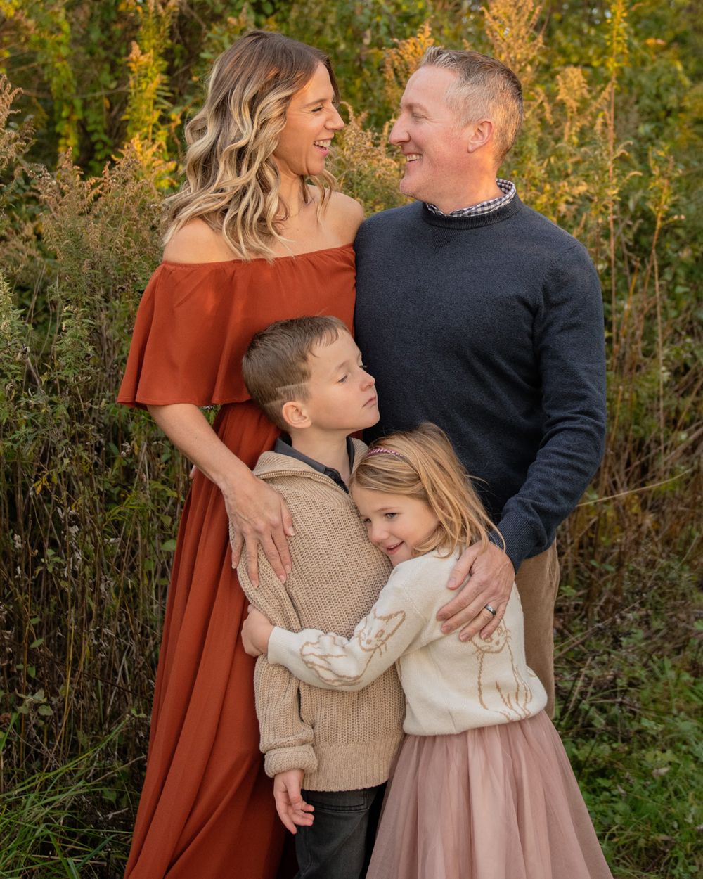 A fall family portrait featuring warm autumn colors with parents and two children embracing outdoors.