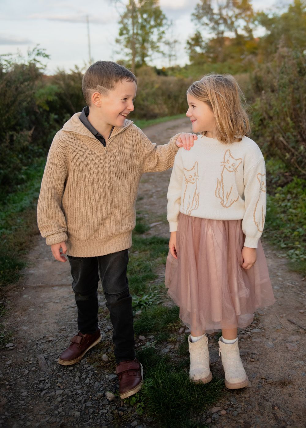 Two children in cozy sweaters share a playful moment on a rustic dirt path.