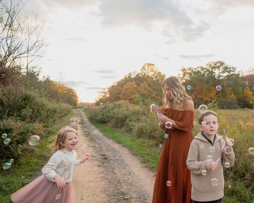 A family blowing bubbles together on a countryside path during sunset.