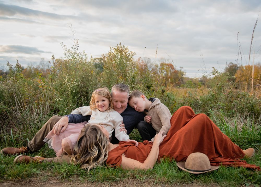 A family cuddles together on a grassy hill during an autumn sunset photo session.
