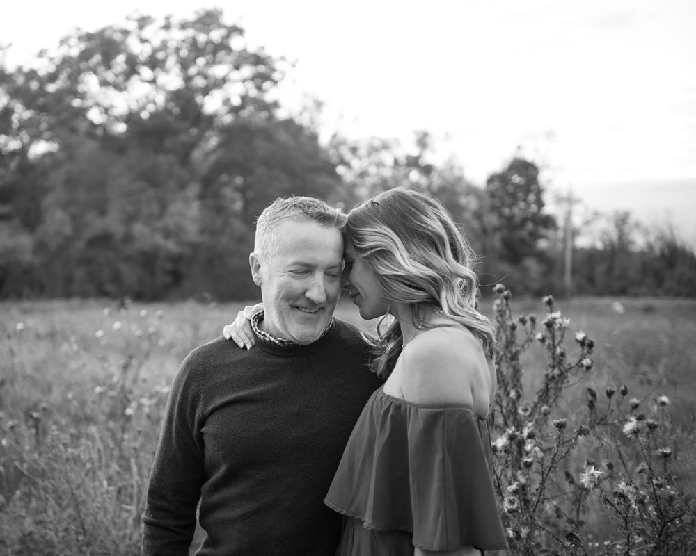A black and white portrait captures a tender moment between a couple in nature.