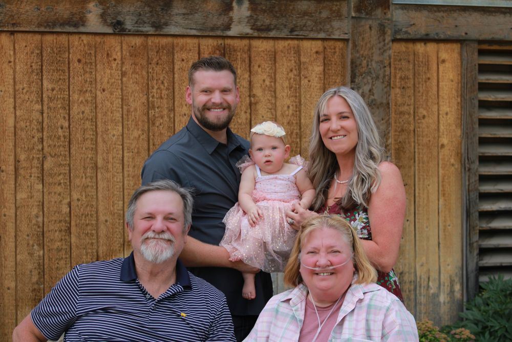 Family portrait with three generations against a wooden barn backdrop.