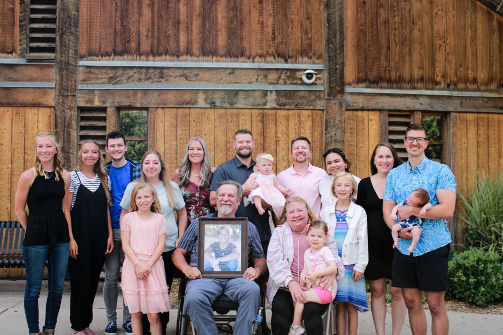 Multi-generational group photo gathered in front of a rustic wooden barn wall.