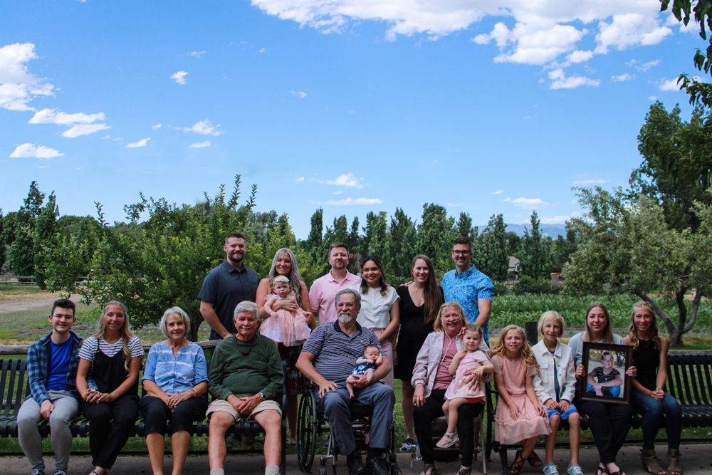 Large family group photo on outdoor bench with mountains and blue sky in background.