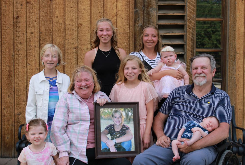 Multi-generational family portrait with framed photo in front of wooden barn structure.