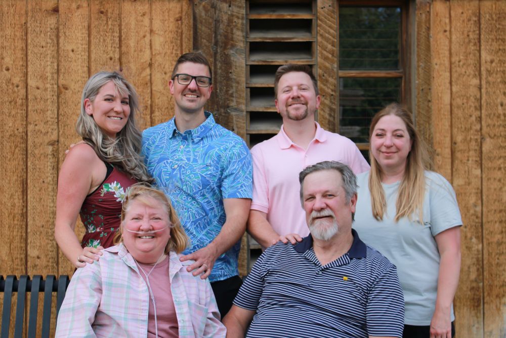 Family group photo against wooden barn siding with casual attire.