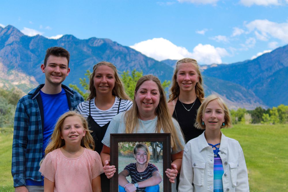 Family portrait with framed photo against mountain backdrop and blue sky.