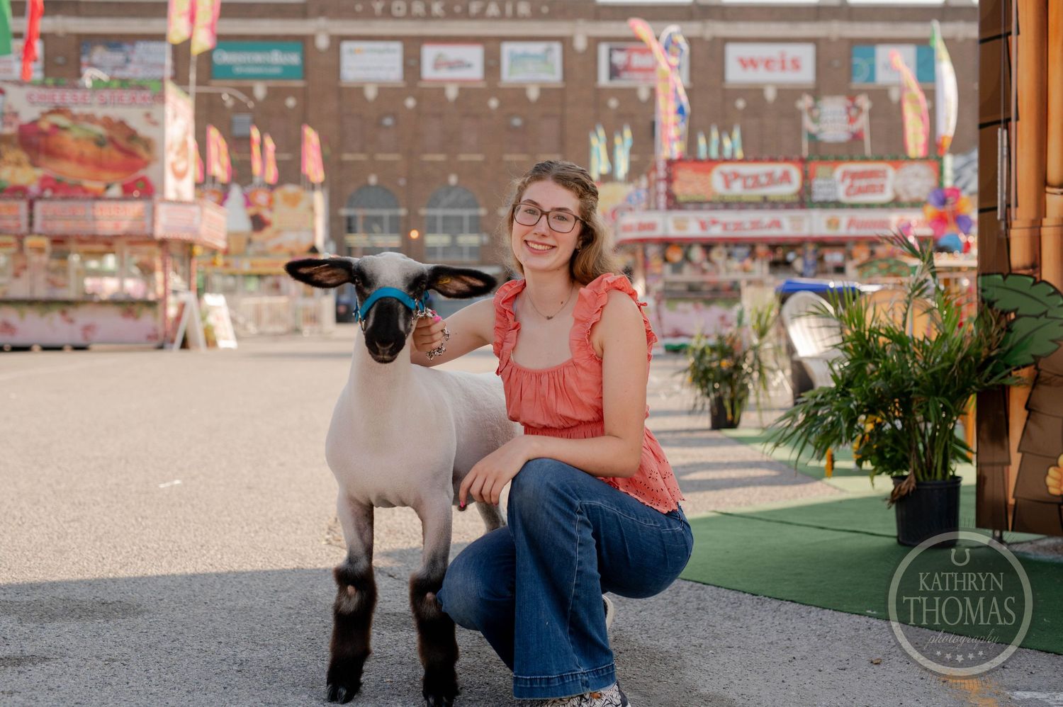 Woman in orange top posing with sheep at a fairground carnival.