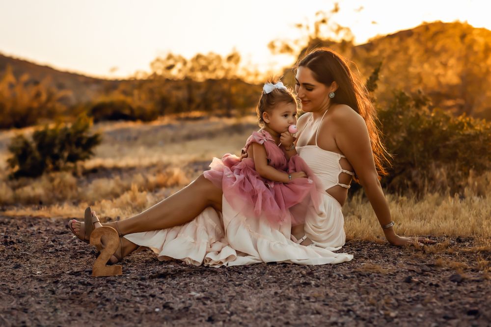 Mother and child in white dress sitting on desert ground at sunset at South Mountain in Phoenix Arizona