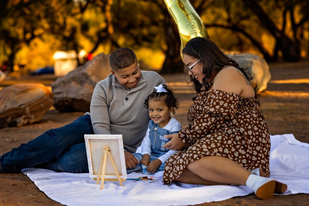 Family having a picnic on blanket while painting together outdoors at sunset near the Salt River in Mesa Arizona for their family photoshoot