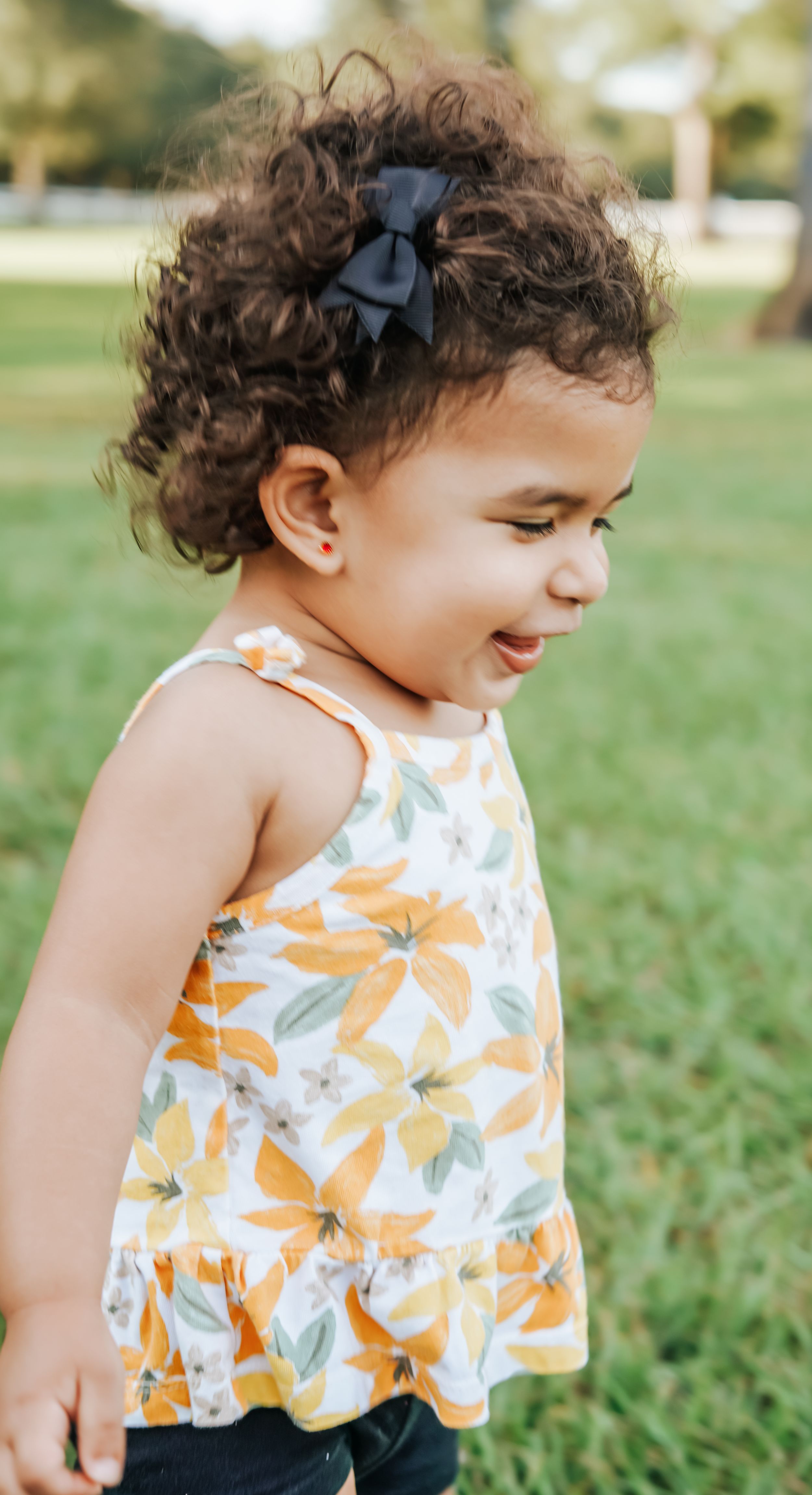 Child wearing orange floral top and shorts plays outdoors in summer.