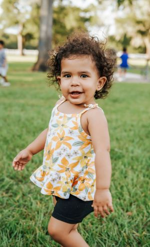 Happy toddler in floral outfit runs and plays in grassy park setting.
