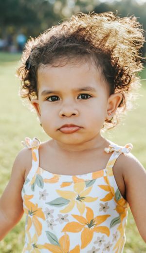 Close up of smiling baby in orange floral tank top outdoors.
