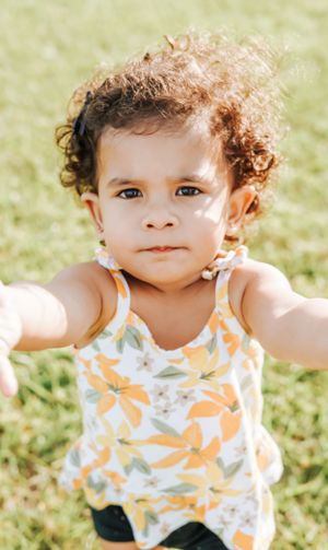 Baby in orange floral tank top making playful expressions on grass.