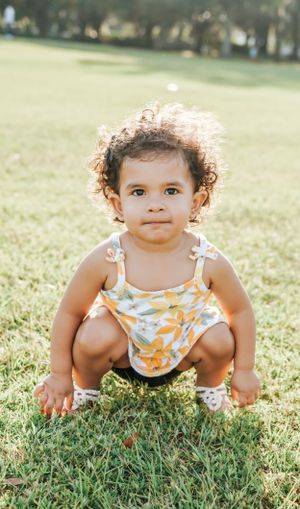 Baby crawling and exploring green grass while wearing orange floral outfit.