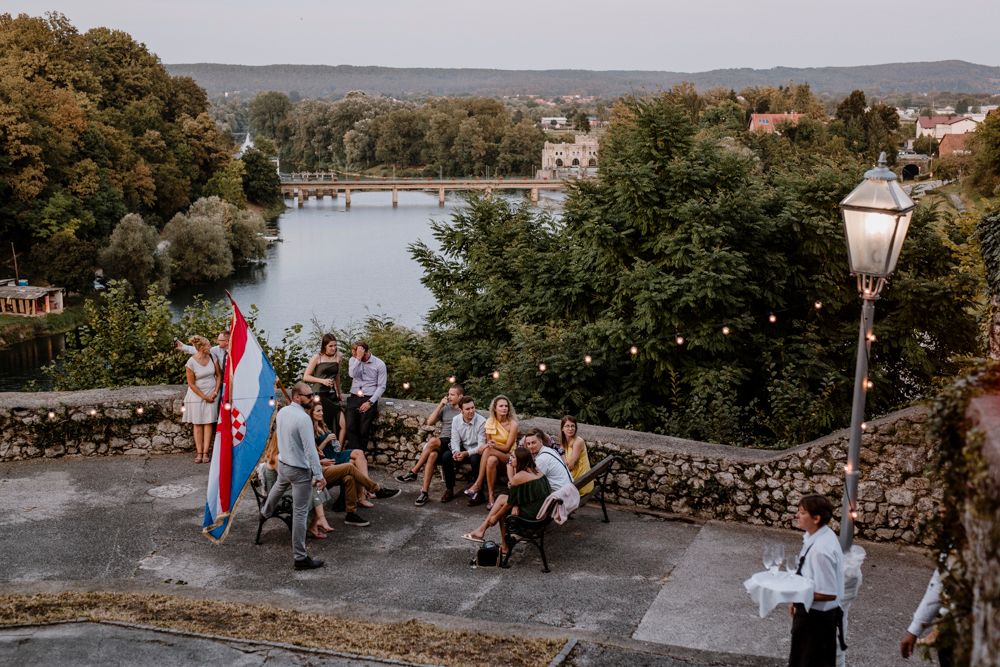 Tourists gather at a scenic viewpoint overlooking a river and autumn trees with a historic lamp post in the foreground.