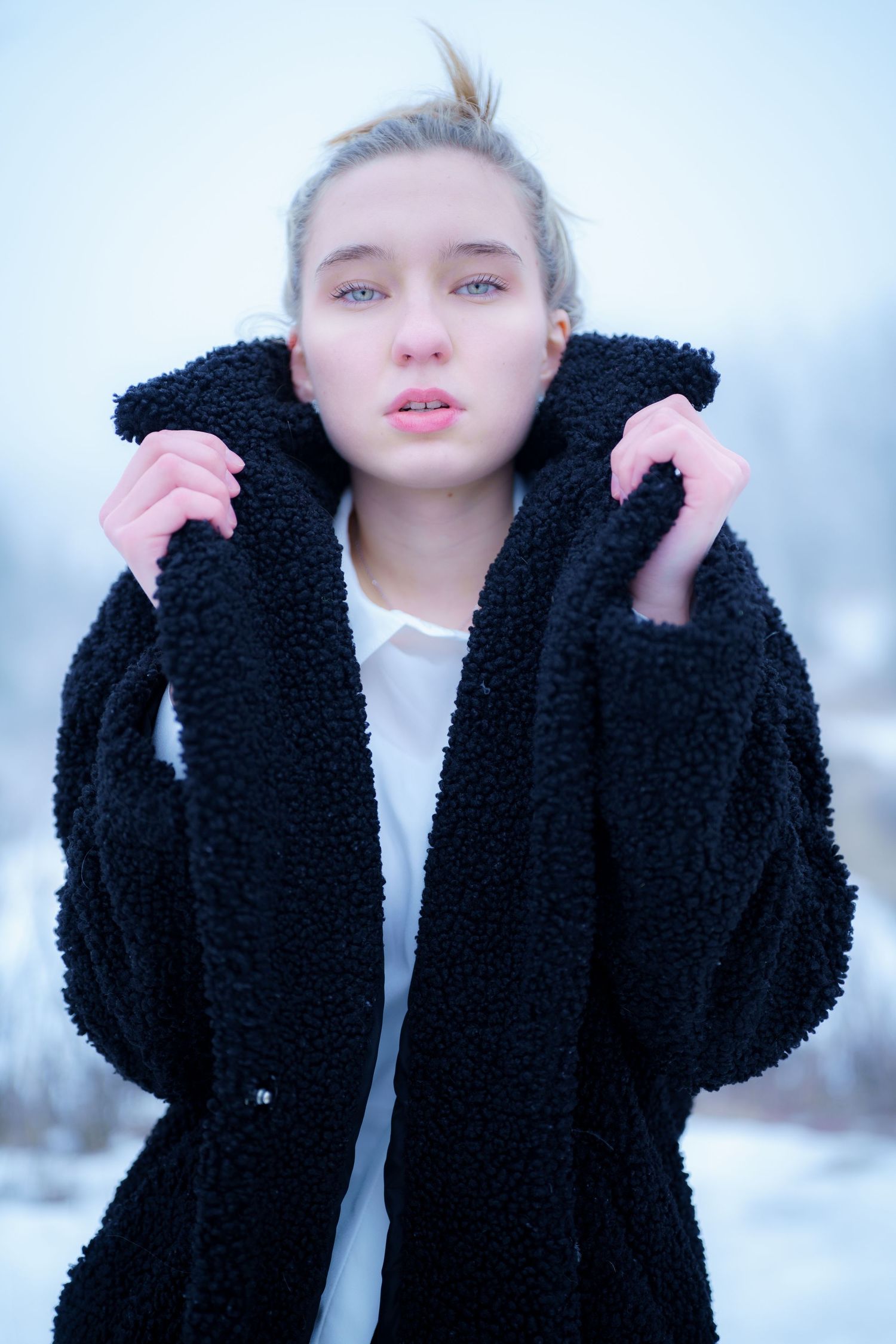Person wearing a cozy black teddy coat poses outside in winter against snowy scenery.