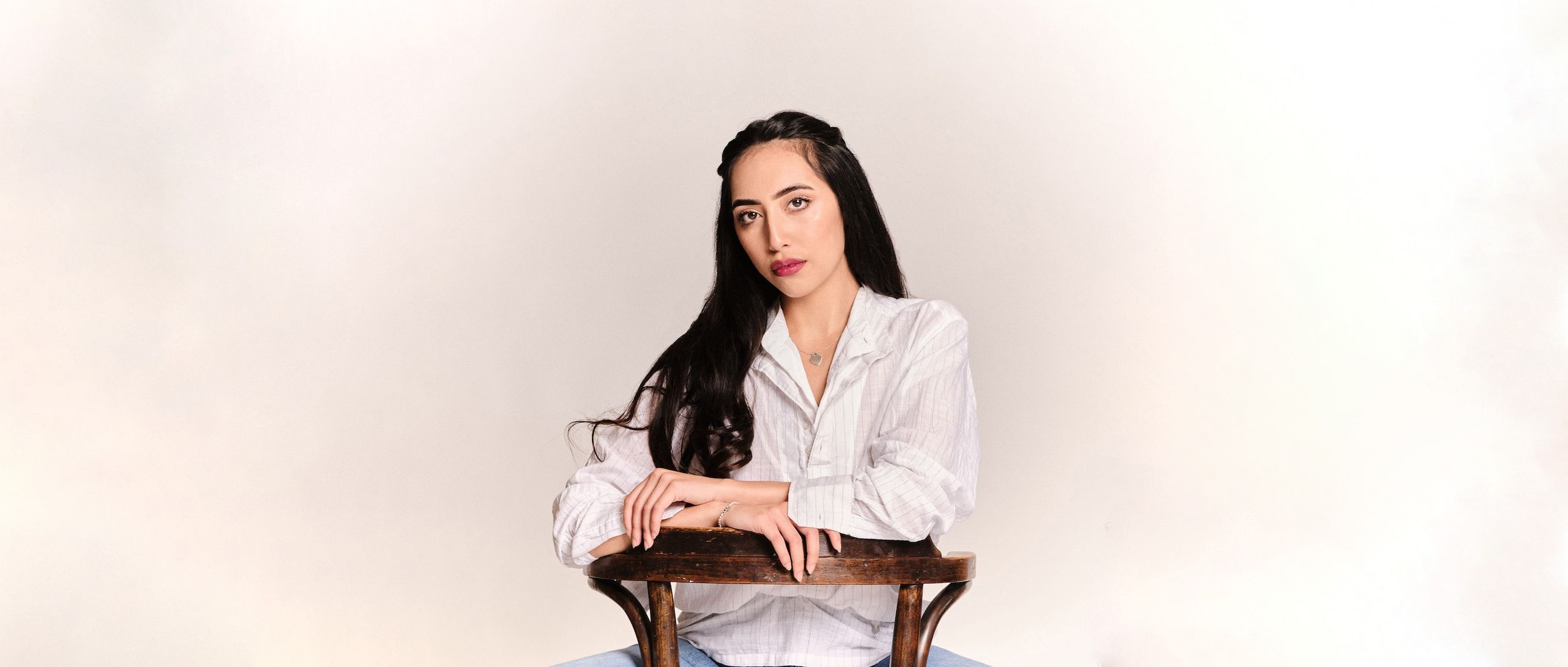 Beautiful boudoir image of a woman in a white shirt. She's relaxed and looking at the camera with dark hair.