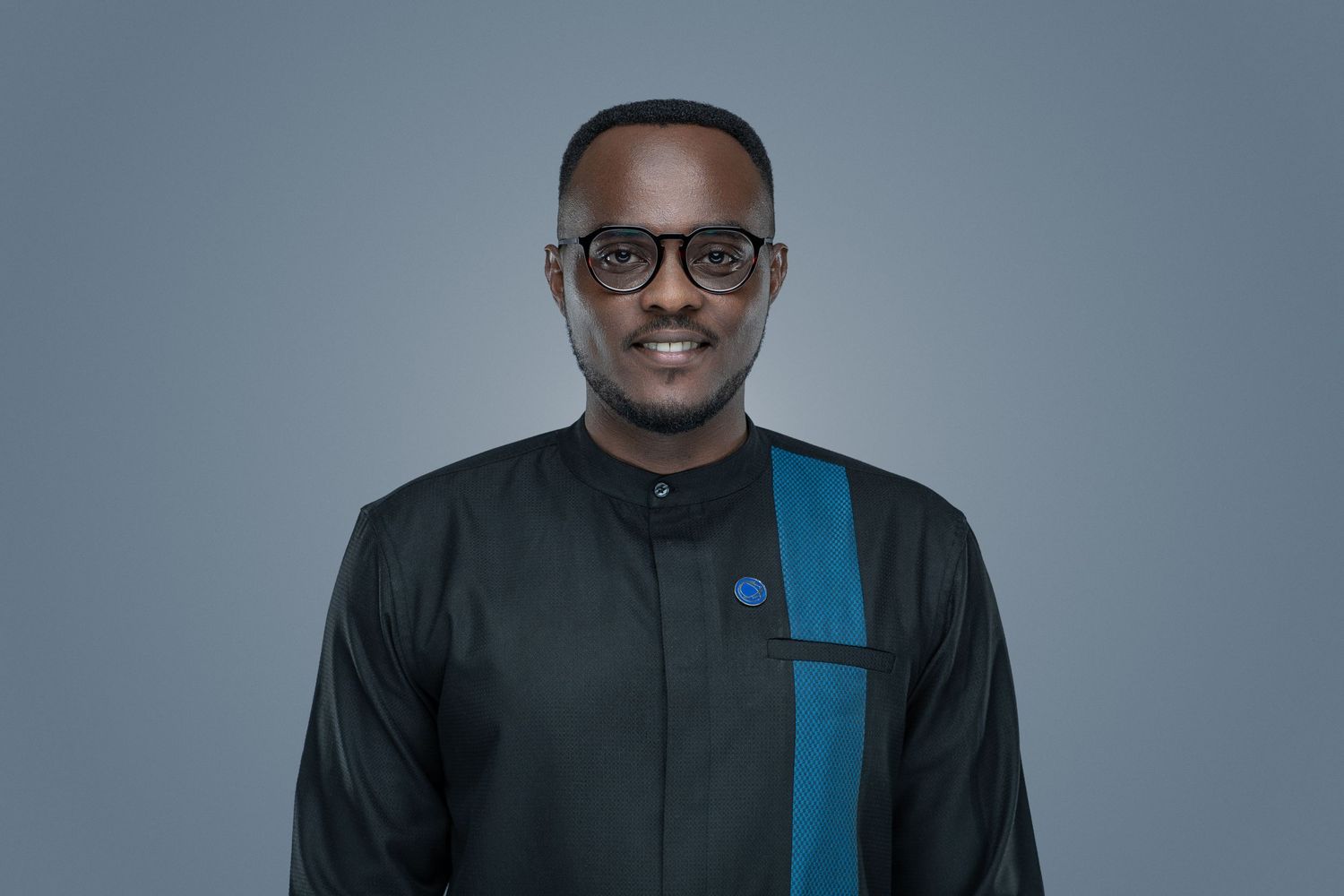 Professional studio portrait of someone wearing glasses and a black shirt with blue accent stripe against grey background.