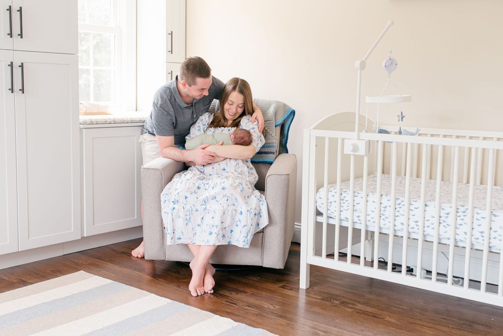Mother holding newborn while father looks on, photographed in a cozy Fair Haven NJ home by a Monmouth County newborn photographer.