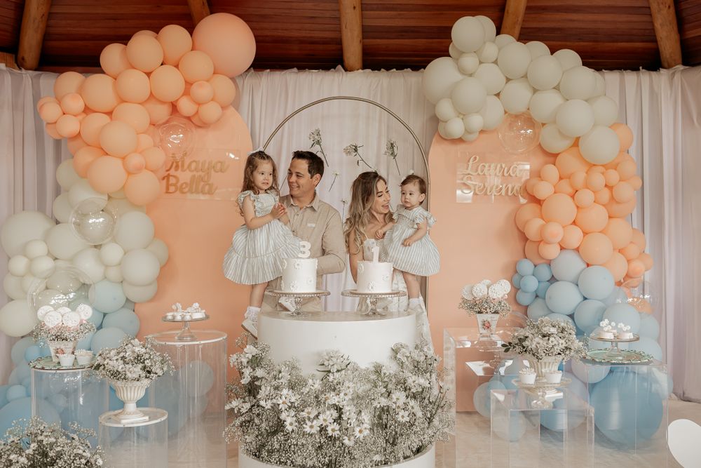 Elegant birthday party setup with peach and blue balloon arches surrounding dessert table with layered cake and floral decor.