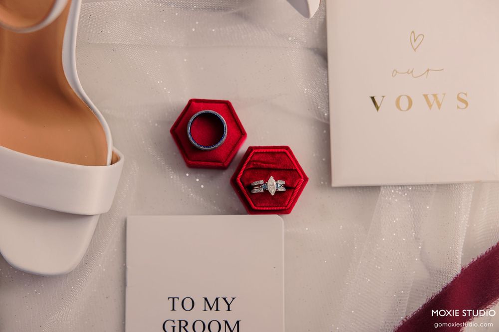 Wedding invitation cards and rings displayed with red hexagonal ring boxes on a beige textured background.
