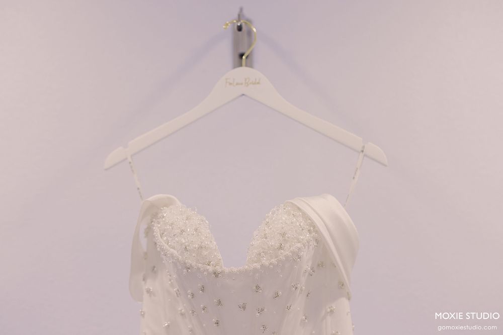 A collection of elegant white wedding dresses displayed on hangers against a light colored wall.