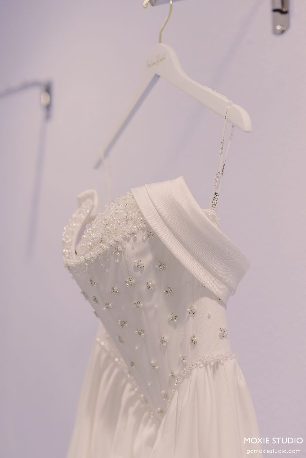 Elegant white wedding dress with beaded bodice hanging on display.