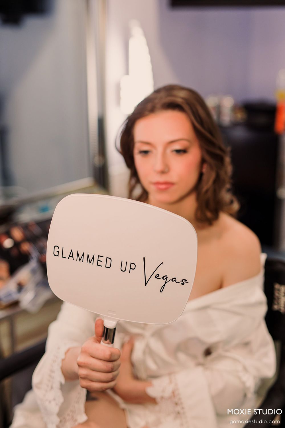 Woman holding a white handheld mirror branded with 'Glammed Up Vegas' during wedding preparations.