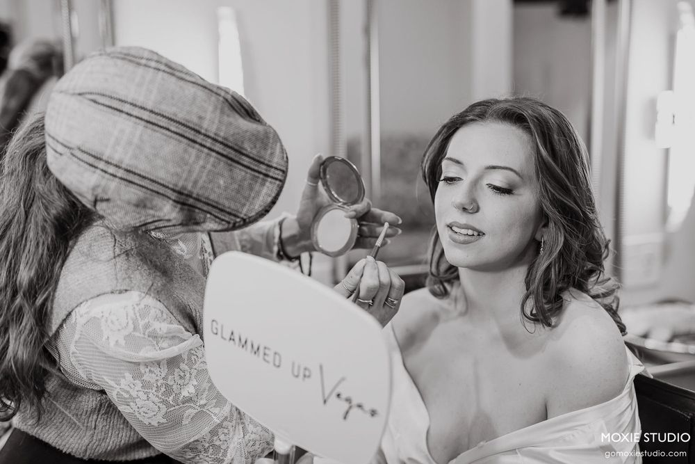 Black and white photo of a makeup artist working on a bride in a white robe.