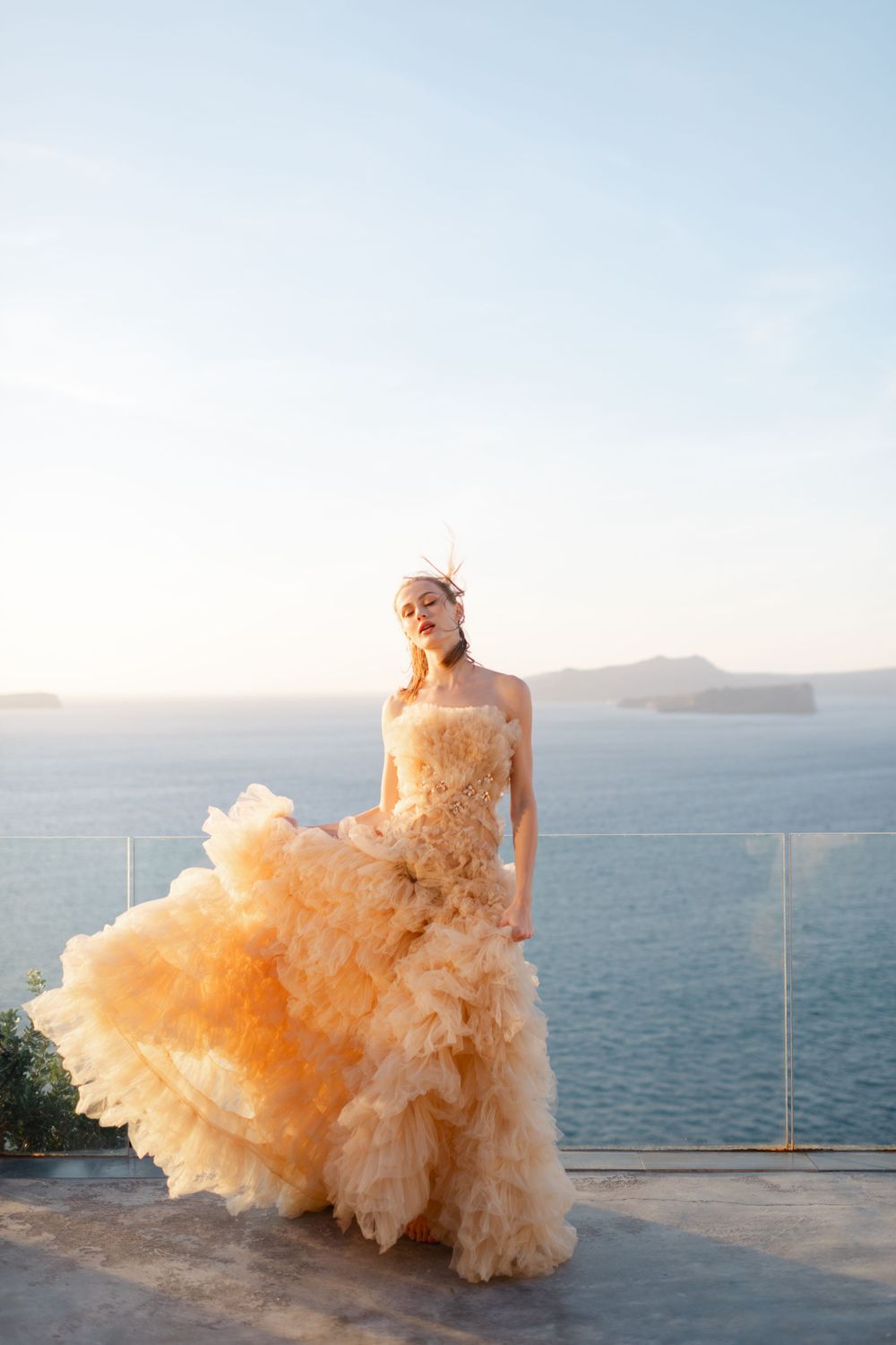 A dramatic peach-colored wedding gown flows in the breeze against a striking ocean backdrop.