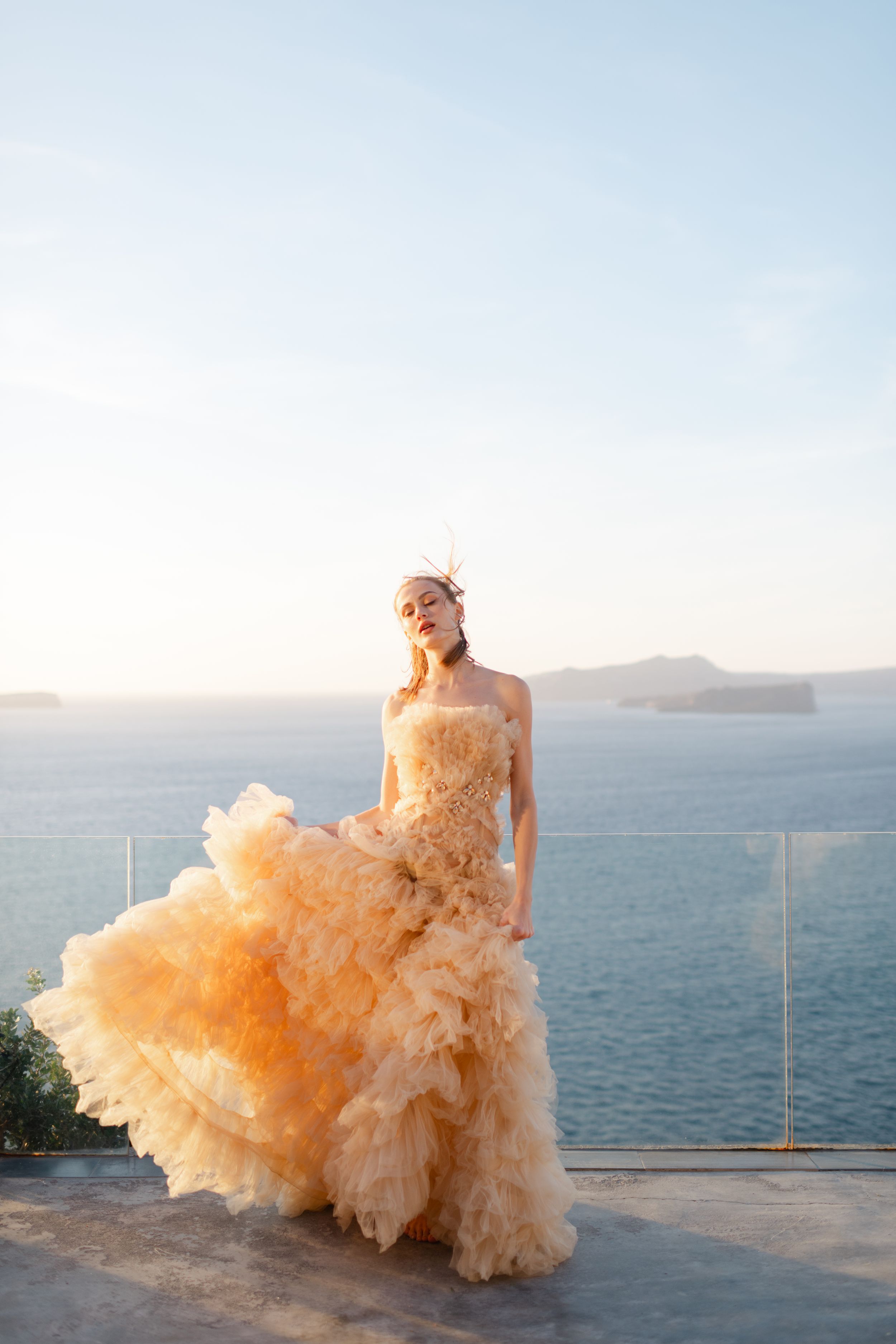 A dramatic peach-colored wedding gown flows in the breeze against a striking ocean backdrop.