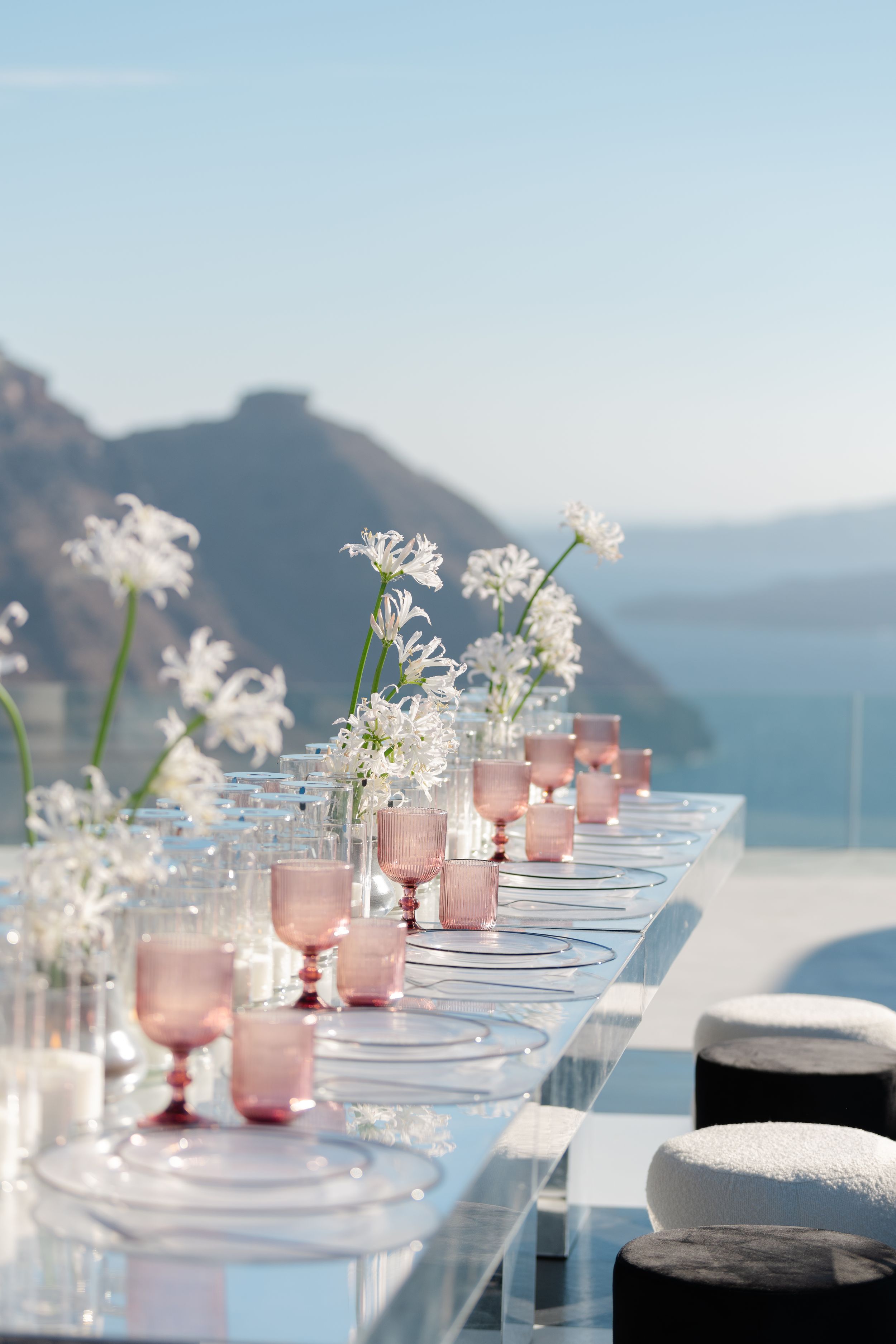 Elegant table setting with pink glassware and white flowers overlooking Mediterranean views.