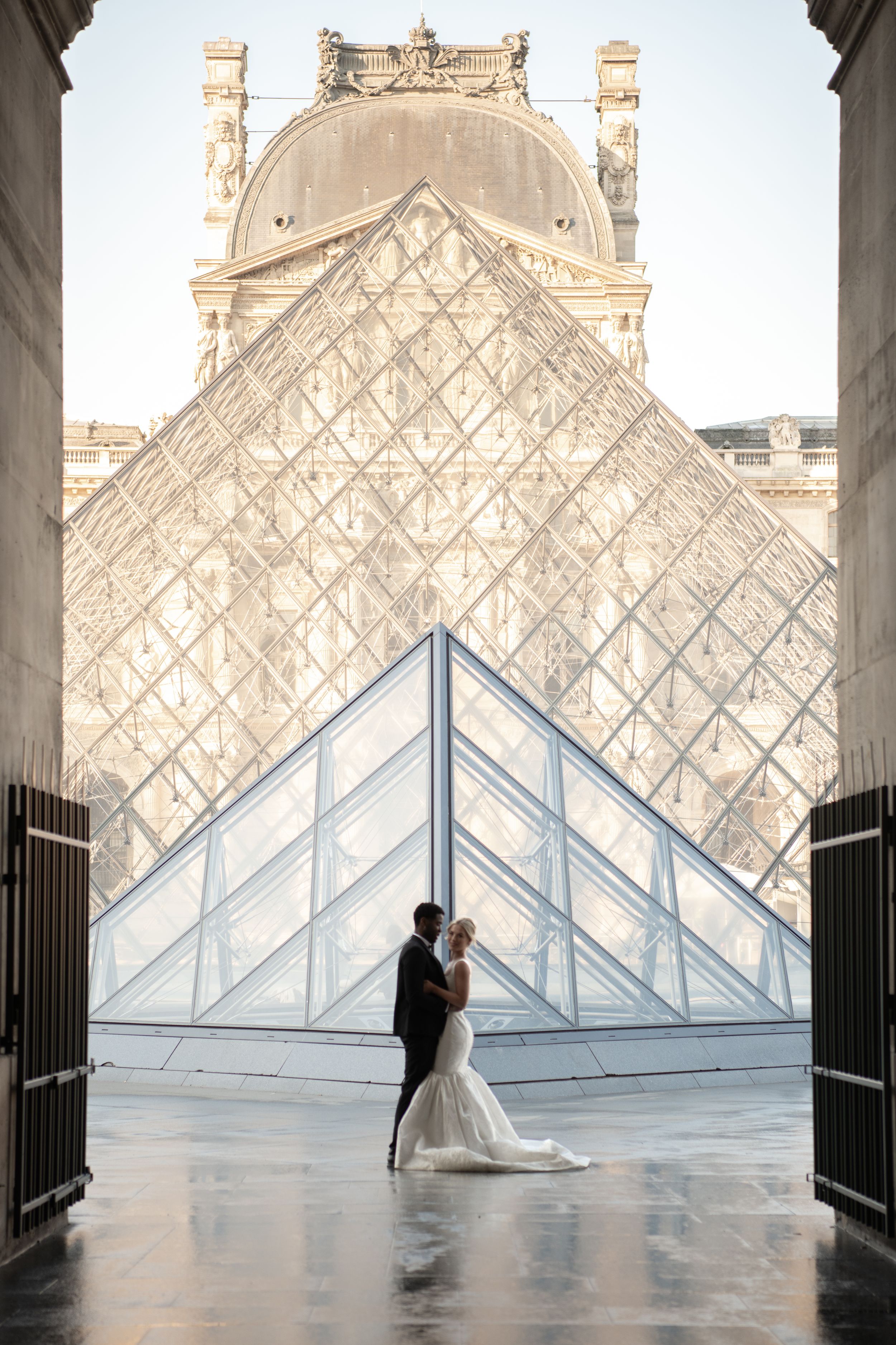Wedding couple poses against iconic glass pyramids of the Louvre Museum in Paris creating romantic silhouettes.